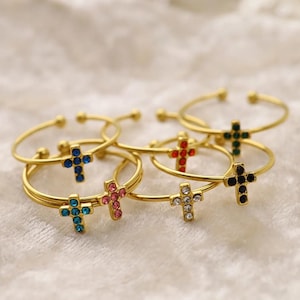 以下が含まれることがあります： 赤、青、緑、ピンク、黒、透明など、さまざまな色の宝石で飾られた十字架のチャームが付いた、ゴールドトーンのバングルブレスレット6個セットです。