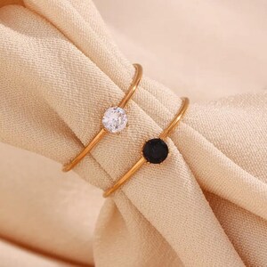 Pode incluir: Dois anéis de ouro com uma pedra redonda branca e uma pedra redonda preta.