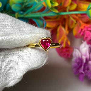 May include: A gold ring with a heart-shaped ruby gemstone.