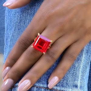 May include: A gold ring with a large, square, red gemstone.