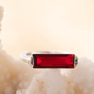 Könnte beinhalten: Ein silberner Ring mit einem rechteckigen roten Edelstein.