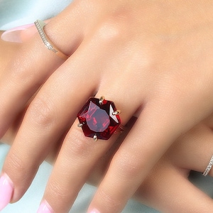 May include: A gold ring with a large, faceted, red gemstone set in a hexagonal shape.