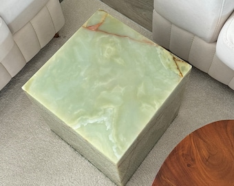 May include: A square green onyx side table with white veining. The table is sitting on a white rug.