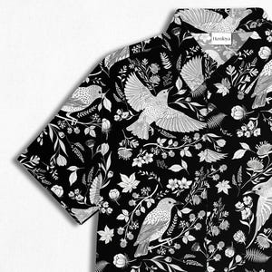 May include: Black button-down shirt with a white bird and floral pattern. The short-sleeved shirt features a classic collar and a detailed all-over print of birds, leaves, and flowers. The shirt is a stylish addition to any wardrobe.