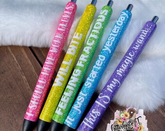 May include: Five glitter pens in a rainbow of colors, each with a different white text phrase. The pens are pink, yellow, green, blue, and purple. The phrases include "SHOULD HAVE WORN GLOVES", "WILL BITE", and "this is my magic wand".