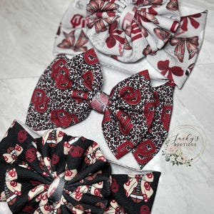 May include: Three fabric headbands featuring textured material. The top headband is white with red bows and footballs. The middle headband has a large bow with a red leopard print and red OU logos. The bottom headband is black with red OU logos and footballs.