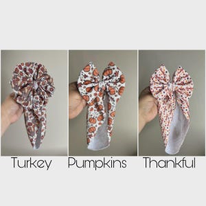 May include: Three fabric headbands with bow accents. The first features a turkey and autumn leaf pattern. The second displays orange pumpkins and leaves. The third has a white background with the repeating text Thankful and colorful dots.