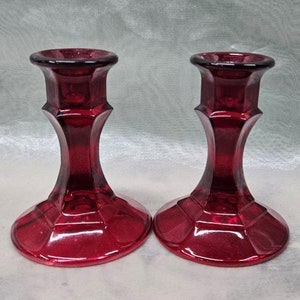 May include: A pair of red glass candle holders with a square base and a fluted design.