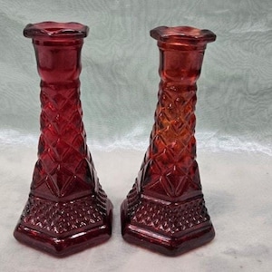 May include: Two red glass candle holders with a diamond pattern. The candle holders are about 6 inches tall.