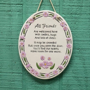 May include: White ceramic plaque with a floral border and the text "All Friends Are welcomed here with smiles, hugs And lots of cheer. It may be crowded But once you open the door, You'll find our hearts Have room for one more."