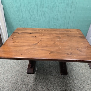 May include: A rectangular wooden table with a warm brown finish. The table has a solid top and is supported by two dark brown pedestal bases. The table is approximately 48 inches long and 36 inches wide.