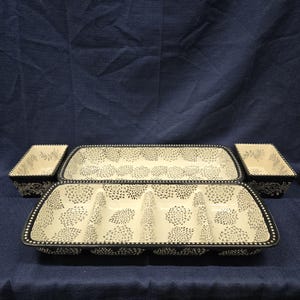May include: A set of four ceramic serving dishes with a cream-colored interior and black floral design. The set includes two rectangular trays and two square bowls, all with a black beaded border.