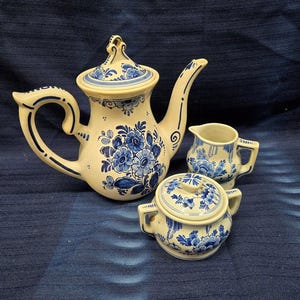 May include: A blue and white Delftware tea set with a teapot, creamer, and sugar bowl. The set features a floral design with blue flowers on a white background.