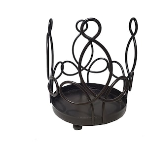 May include: A black metal candle holder with a decorative swirl design. The holder has a round base and a circular opening for a candle.
