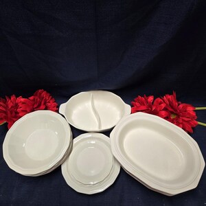 Könnte beinhalten: Eine Sammlung weißer Keramik-Servierschalen, darunter Schalen, Teller und eine geteilte Schale. Das Geschirr hat ein schlichtes, elegantes Design und ist auf einer dunkelblauen Oberfläche mit roten Blumen angeordnet.