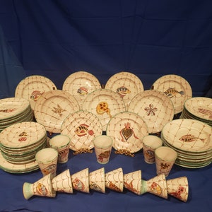 May include: A set of white ceramic dinnerware with a green rim and a fishnet design. The set includes plates, bowls, and cups, all featuring colorful fish illustrations.