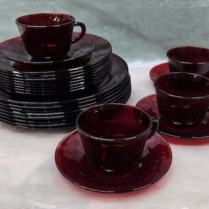 Puede incluir: Un juego de vajilla de vidrio rojo rubí con una pila de platos y cuatro tazas y platillos.