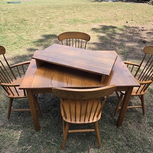 May include: A wooden dining set consisting of a rectangular table with a removable top riser and four matching spindle-back chairs. The furniture features a medium-brown wood grain finish, straight legs on the table, and curved backrests.