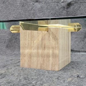 May include: A modern coffee table featuring a rectangular glass top supported by a light-colored, block-shaped wooden base. The table has gold-colored metal accents and measures approximately 48 inches long.