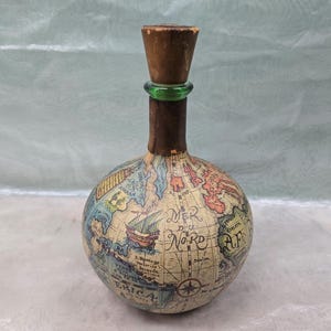 May include: A vintage glass bottle shaped like a globe with a cork stopper and a green glass neck. The bottle is decorated with a world map and the text "Mer du Nord".