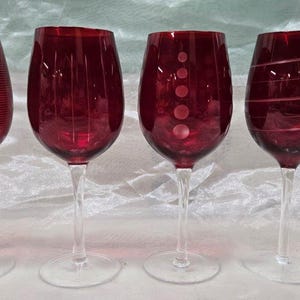 Puede incluir: Juego de cuatro copas de vino tinto con diferentes diseños grabados. Cada copa tiene un tallo y una base transparentes.