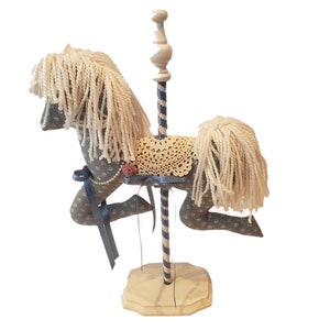May include: A gray and white fabric carousel horse with a white yarn mane and tail. The horse is mounted on a wooden base with a striped pole.