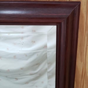 May include: A rectangular mirror with a dark mahogany wood frame. The mirror is reflecting a white surface with a subtle pattern.