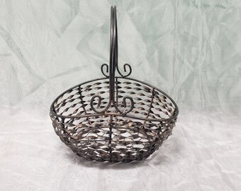 Puede incluir: Una cesta de metal negro con un diseño de alambre retorcido y un asa. La cesta es de forma ovalada y tiene un diseño de desplazamiento decorativo en el asa.