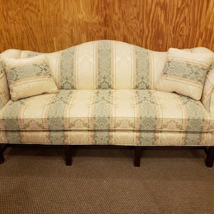 May include: A vintage sofa with a cream, green, and beige floral pattern. The sofa has two matching throw pillows and dark wooden legs. The arms are curved, and the back is arched.