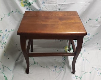 May include: A small, square wooden side table with a rich, warm brown finish. The table features a flat top and curved legs, connected by a lower stretcher for added stability. A classic piece of furniture.
