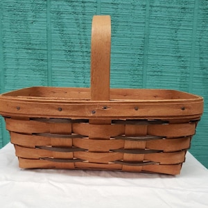 May include: A brown woven basket with a wooden handle. The basket has a rectangular shape and is made of natural materials.