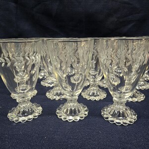 May include: A collection of clear glass goblets featuring a delicate etched leaf pattern around the upper rim. Each goblet stands on a short, thick stem with a circular base decorated with a distinct beaded or hobnail edge design.