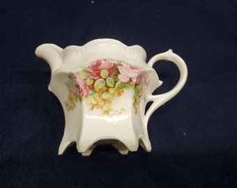 Jarra de vidrio con estampado floral, fondo blanco y base con patas