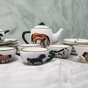 Peut inclure: Un service à thé en porcelaine blanche avec des finitions vertes et des illustrations de chevaux. L'ensemble comprend une théière, un pot à crème, un sucrier, quatre tasses et quatre soucoupes.