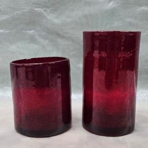 May include: Two red glass candle holders, one taller than the other, with a textured surface.