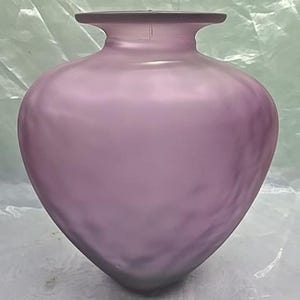 May include: A lilac-coloured vase with a rounded body and a flared rim. The glass has a textured surface, and the vase has a heart-like shape. The vase is an elegant decorative item.