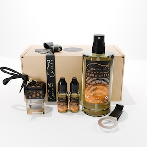 Op de afbeelding: Een cadeaupakket met auto-luchtverfrissers. Inclusief een spuitfles, twee navullingen voor de diffuser, een ventilatieclip en een decoratieve hangende diffuser. De doos en accessoires zijn zwart, bruin en transparant.