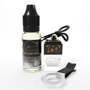 Puede incluir: Un juego de ambientador para coche con un frasco de recarga, un difusor de madera y una pinza de ventilación. El frasco de recarga es transparente con una tapa negra y una etiqueta que dice "Car Elixir Luxury Car Fragrance Diffuser Refill". El difusor es negro con diseño de vetas de madera.