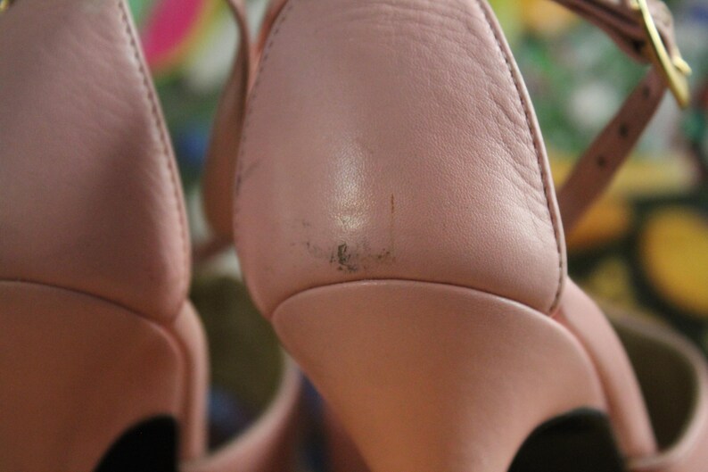 May include: Close-up of a pair of pink leather high-heeled sandals. The sandals have a strap around the ankle and a gold-colored buckle. The leather shows some wear and tear.