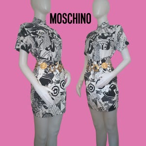 May include: A black and white short-sleeved dress with a newspaper print design. The dress has a gold belt with a large buckle. The dress is labeled "MOSCHINO".