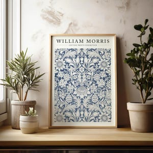 Puede incluir: Una impresi&oacute;n enmarcada de un patr&oacute;n floral azul y blanco con el texto "WILLIAM MORRIS - COTTON PRINTS EXHIBITION" en la parte superior.