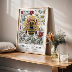 May include: A framed print of a bee surrounded by flowers. The print is titled "William Morris: A History of British Design" and is from the Cotton Prints Exhibition at The National Gallery, UK.