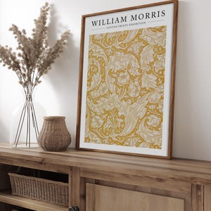 May include: A framed print with a yellow background and a white floral pattern. The print has the text "WILLIAM MORRIS COTTON PRINTS EXHIBITION" at the top.