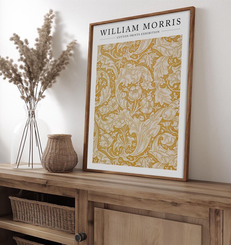 May include: A framed print with a yellow background and a white floral pattern. The print has the text "WILLIAM MORRIS COTTON PRINTS EXHIBITION" at the top.