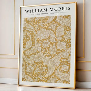May include: A gold framed poster with the text "WILLIAM MORRIS - COTTON PRINTS EXHIBITION" at the top. The poster features a repeating pattern of white stylized leaves and flowers on a yellow background.
