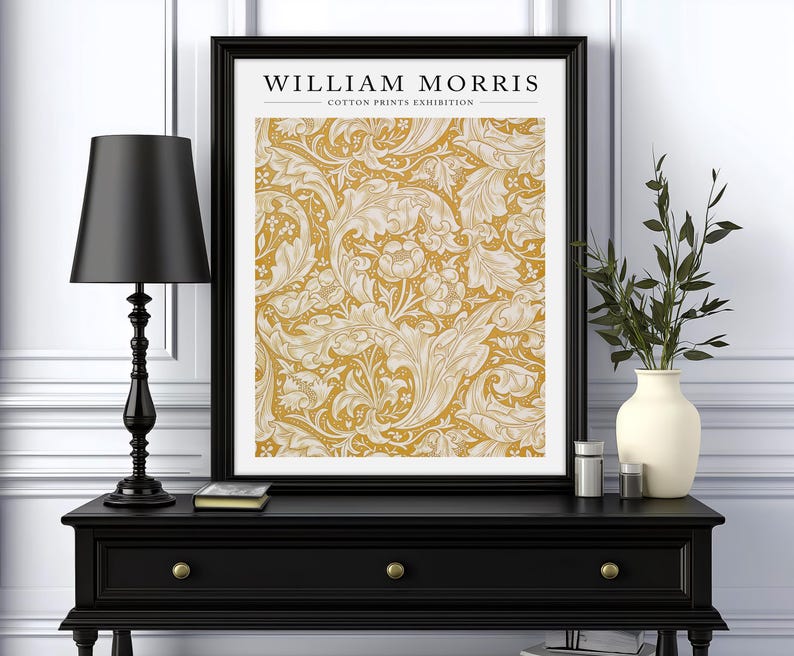 May include: A black framed print with the text "WILLIAM MORRIS - COTTON PRINTS EXHIBITION" and a yellow and white floral pattern.
