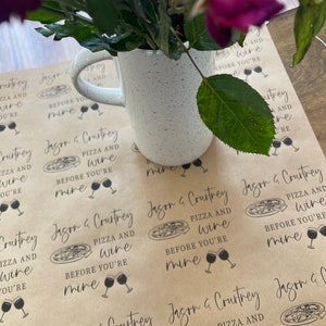 May include: Brown paper gift wrap with a repeating pattern of pizza slices and wine glasses. The text on the paper reads "Jason & Courtney Pizza and Wine Before You're Mine".