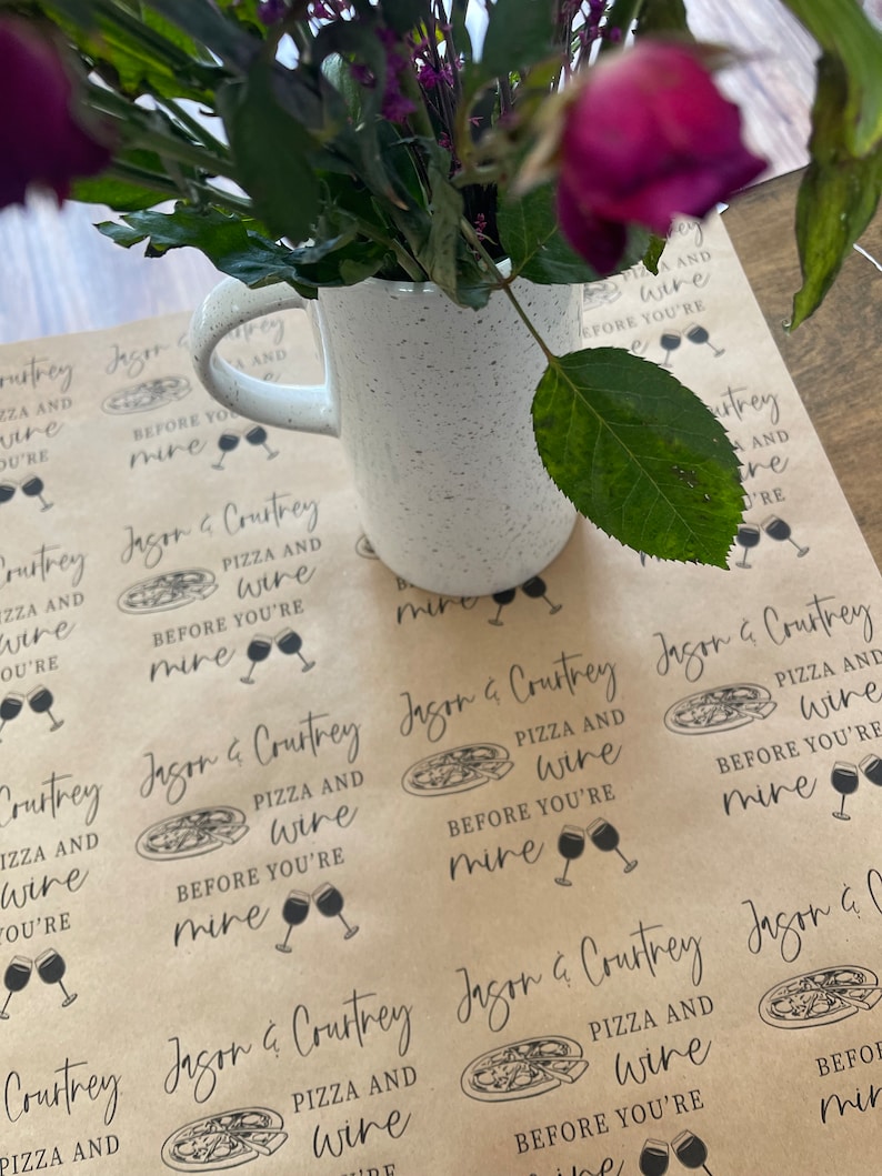 May include: Brown paper gift wrap with a repeating pattern of pizza slices and wine glasses. The text on the paper reads "Jason & Courtney Pizza and Wine Before You're Mine".