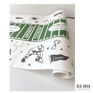 May include: Rolled white paper with a green and black football field design. The design includes the words "Touchdown!", "Game Day at the Cash House", and "Lions". Also includes a football player and trophy.