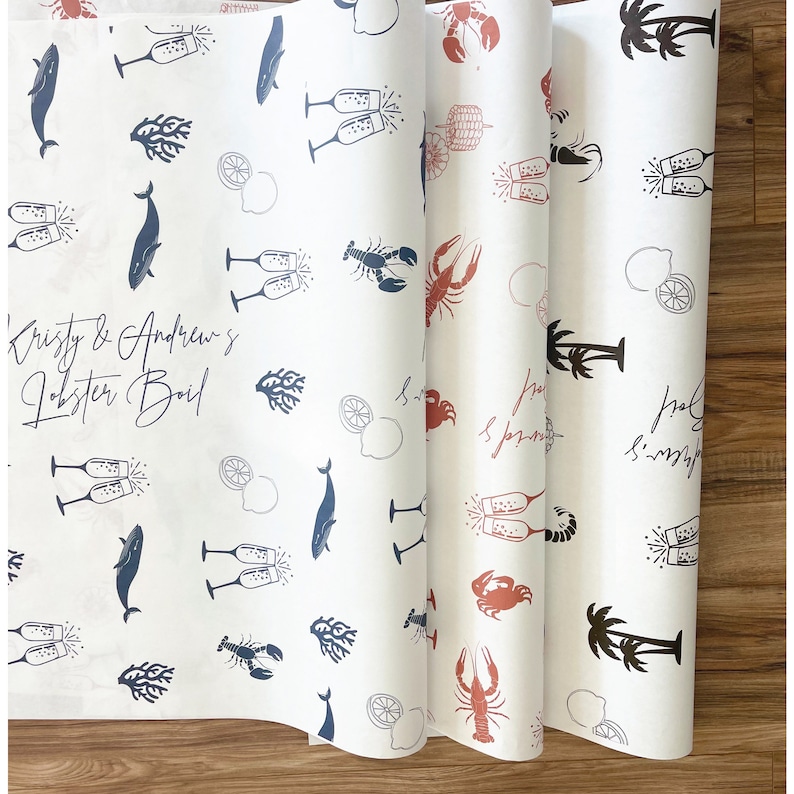 K&ouml;nnte beinhalten: Wei&szlig;es Geschenkpapier mit einem sich wiederholenden Muster aus Hummern, Zitronen, Sektgl&auml;sern, Palmen und Walen. Der Text "Kristy & Andrew's Lobster Boil" ist oben auf dem Papier in Schwarz gedruckt.